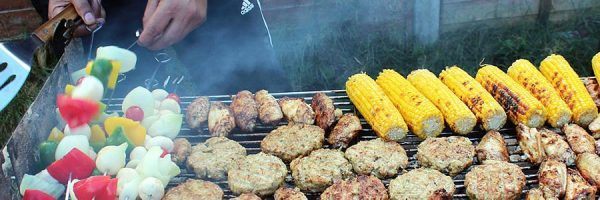 Vegetable skewers, corn on the cob, and meats on a barbeque.