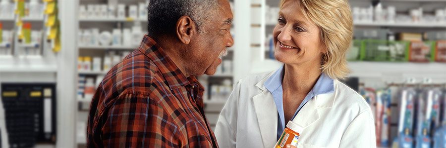An older African-American man talks to a Caucasian female pharmacist as she explains his prescription.