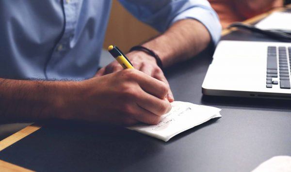 person writing notes in front of computer
