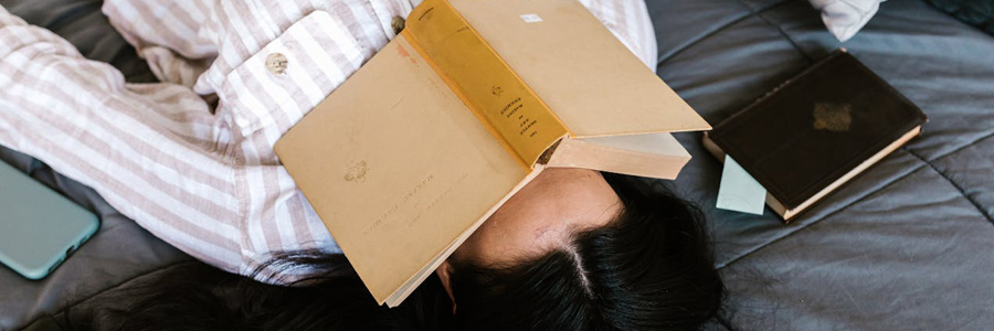 Person lying in bed with book on their face