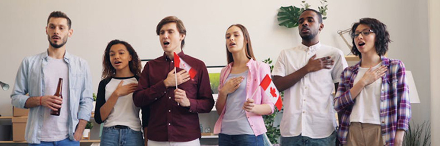 A group of multicultural people holding small Canadian flags and singing the anthem